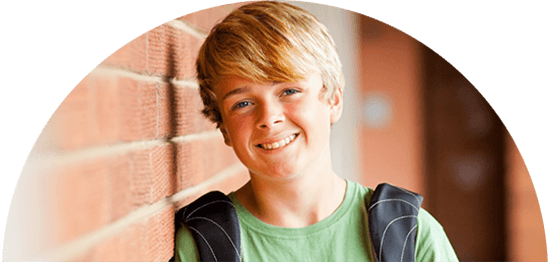 Boy with backpack leaning against brick wall at school