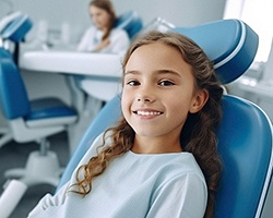 Child in blue shirt smiling while sitting in dental chair