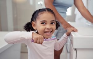 child smiling while brushing her teeth