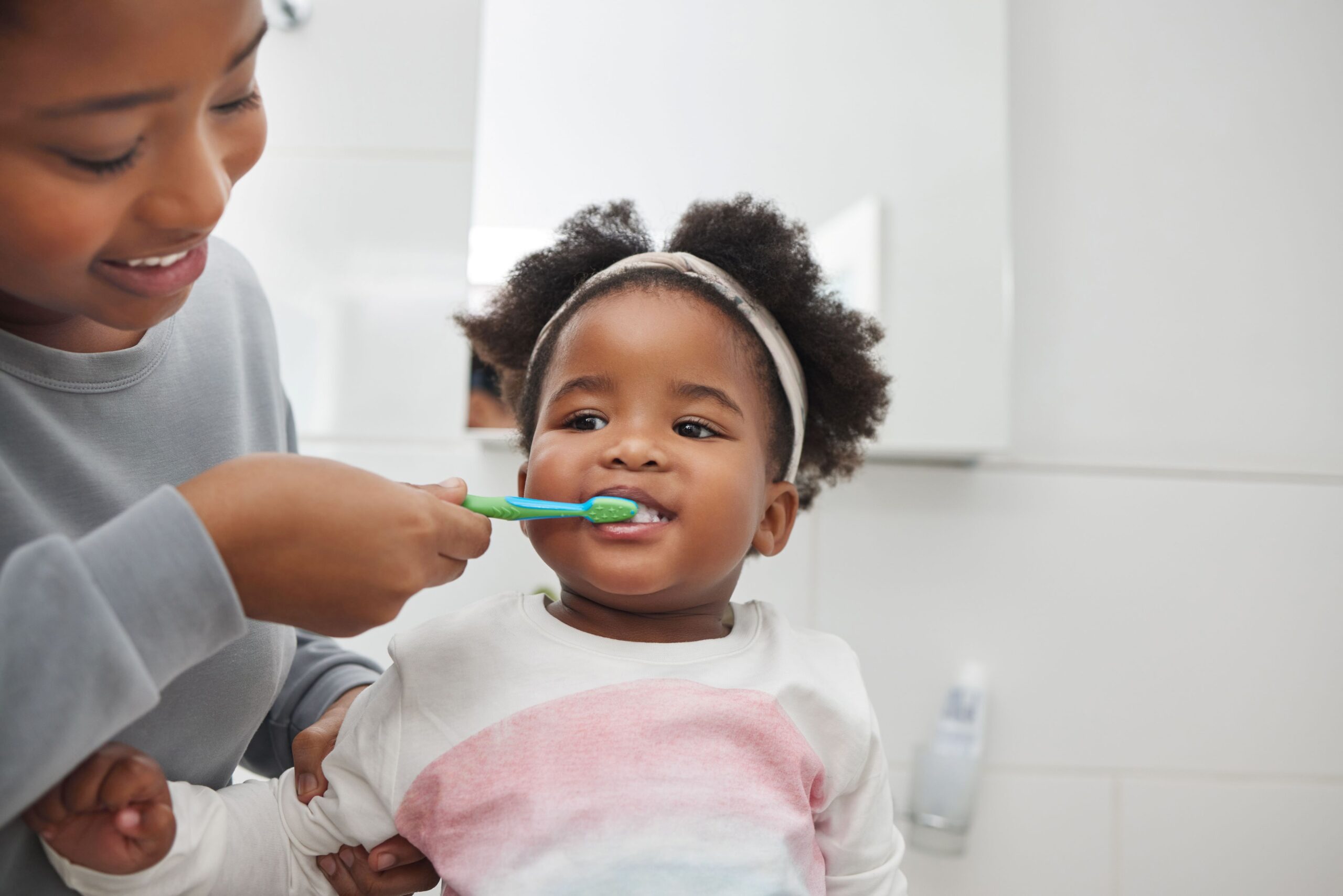 Woman brushing little girl's teeth with a green and blue toothbrush.