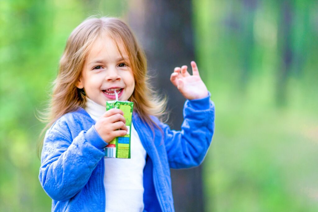 Young girl in blue sweater raising hand and sipping from juice box