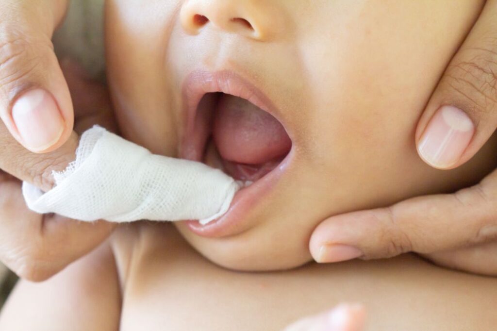 A mother cleaning a baby’s gums with a cloth